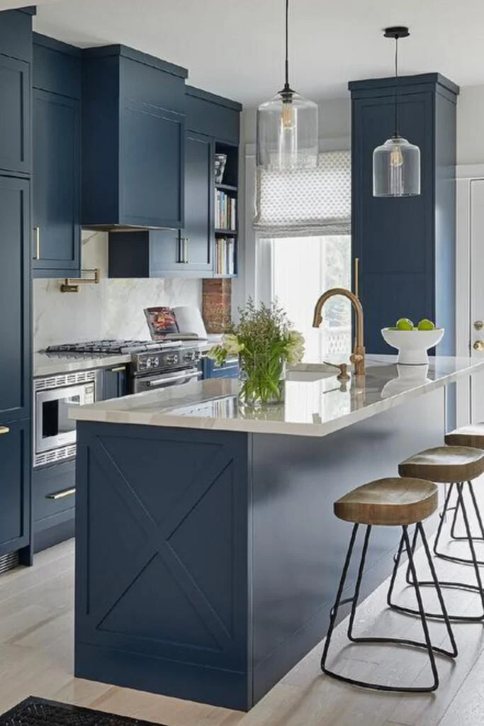A kitchen with cabinets painted in a medium grayish blue.  The countertops are white marble and natural wood and metal stools sit at the bar.