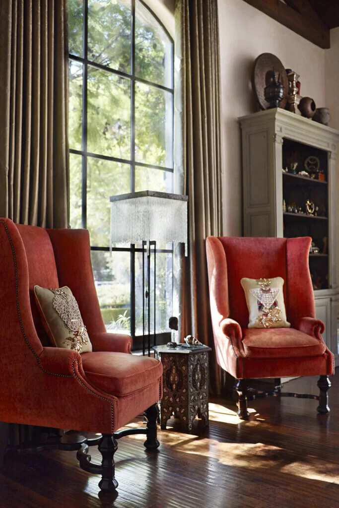 Burnt orange colored wingback chairs frame a large arched window.  The chairs are adorned with beaded pillows.